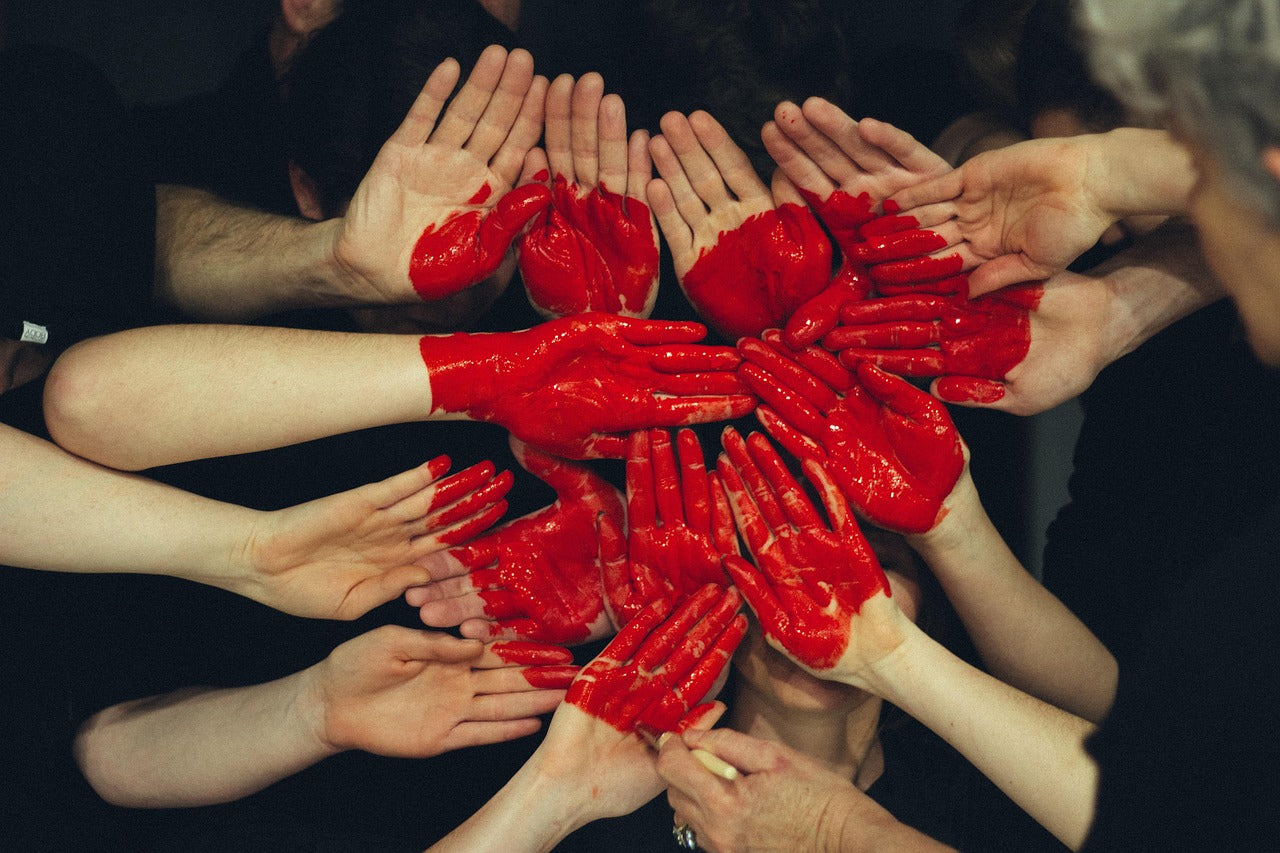 Multiple hands held out with a red heart painted on them