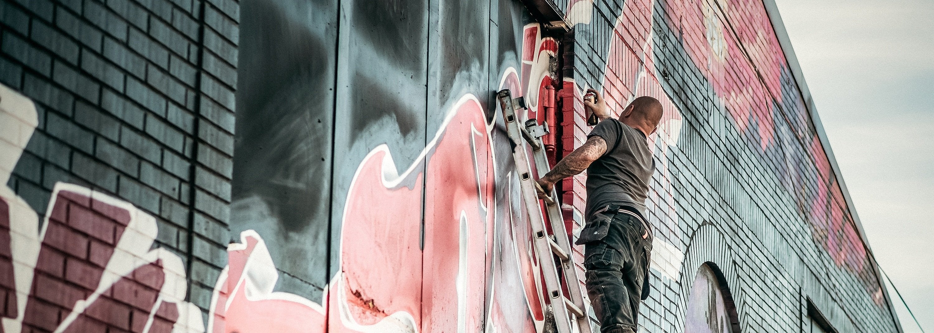 Person painting a large mural on a brick wall