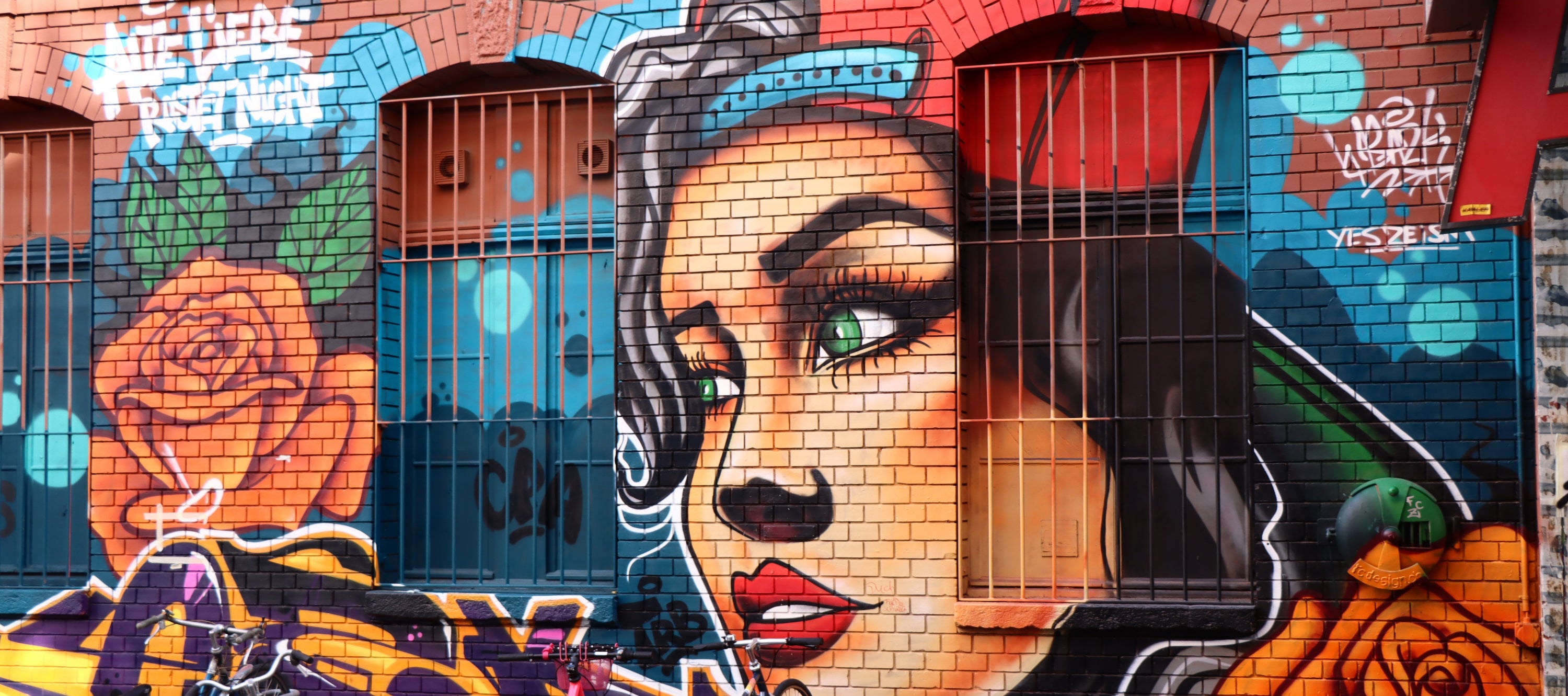 Mural of a woman's face on a brick wall with colorful graffiti.