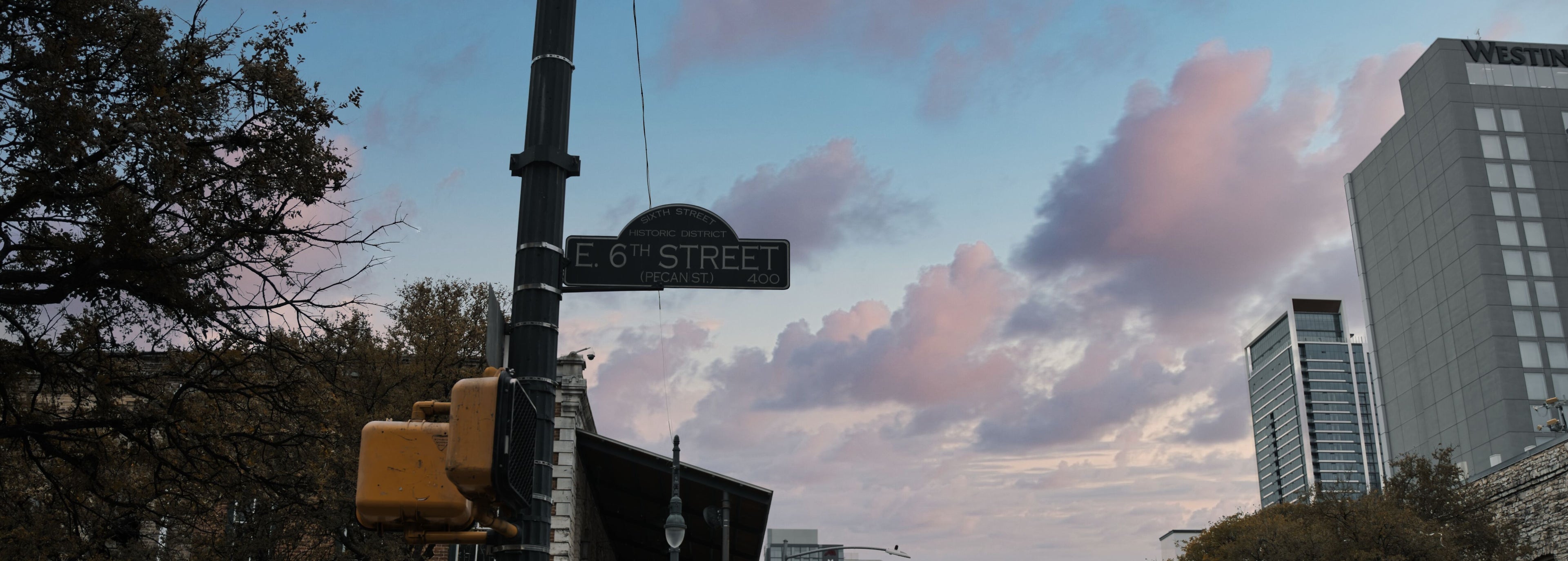City street scene with buildings, trees, and a cloudy sky.