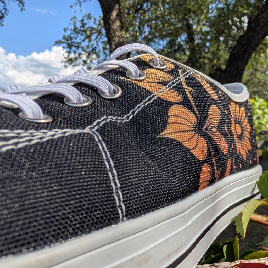 Black sneaker with orange mandala pattern on a blurred natural background